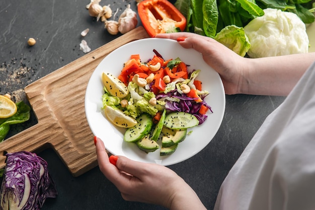 Salada de vegetais frescos em mãos femininas contra o fundo de uma mesa escura