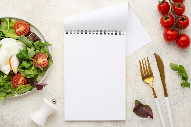 Salada de vista superior com tomate e ovo frito com bloco de notas em branco