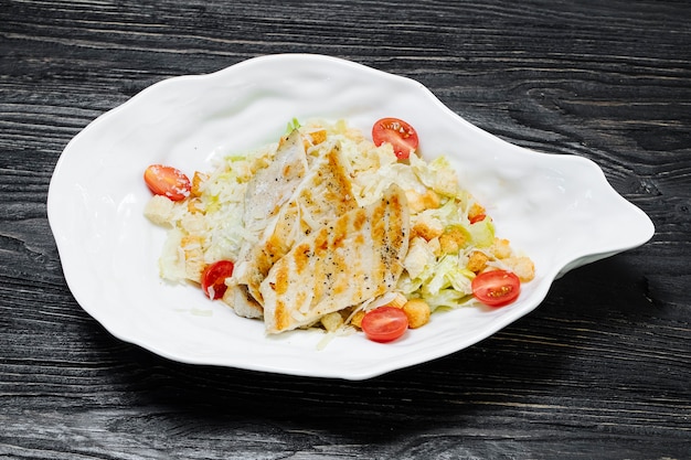 Salada grega com carne branca, alface e tomate cereja dentro de chapa branca.