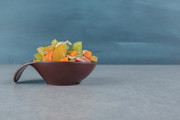 Salada mista de vegetais em um copo de madeira na mesa de concreto.