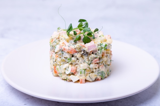 Salada olivier em um prato branco, decorado com brotos de ervilha. salada russa.