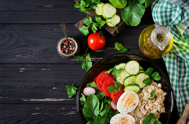 Salada saudável de legumes frescos - tomate, pepino, rabanete, ovo, rúcula e aveia na tigela. Dieta alimentar. Postura plana. Vista do topo