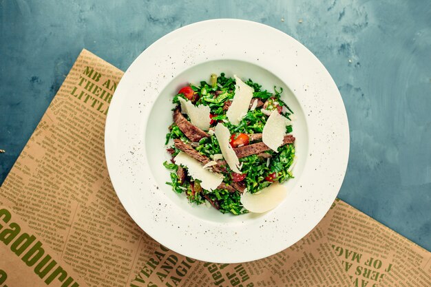 Salada verde com carne e queijo picado dentro da tigela branca.