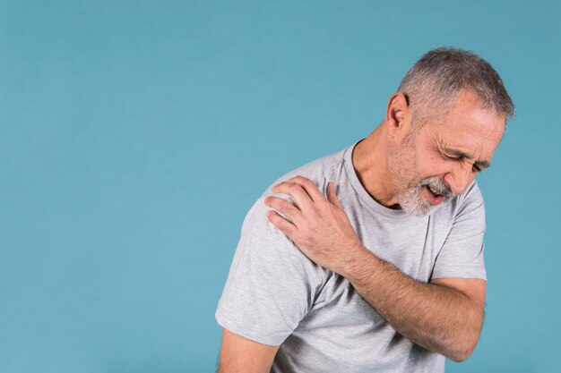 Salientou o homem sênior com dor no ombro em pano de fundo azul