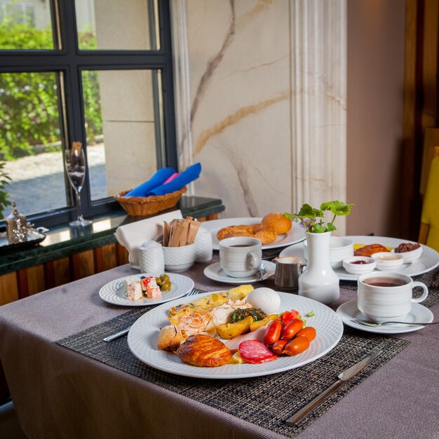 Salsichas de café da manhã, ovo cozido, omelete, croissant em pratos e xícara de chá na mesa