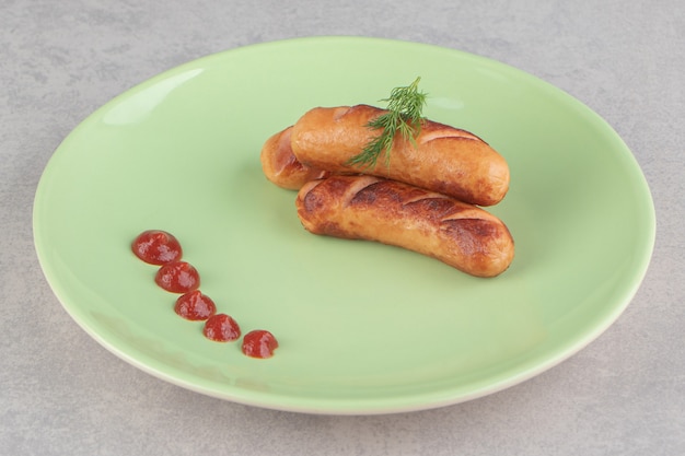 Salsichas fritas saborosas e ketchup na placa verde.