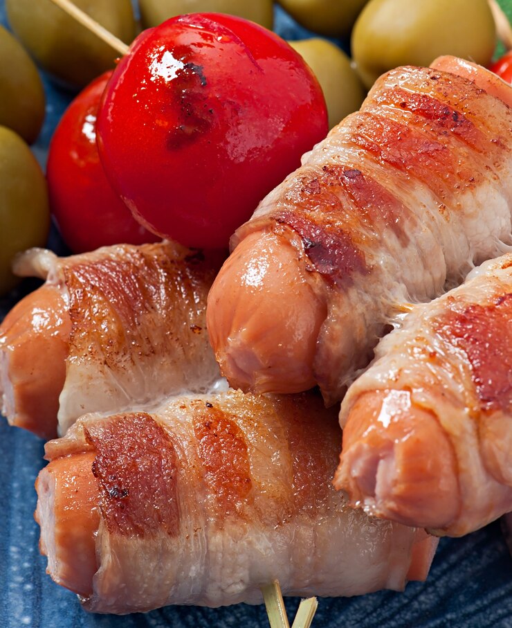 Foto grátis salsichas grelhadas envoltas em tiras de bacon com tomate e folhas de sálvia