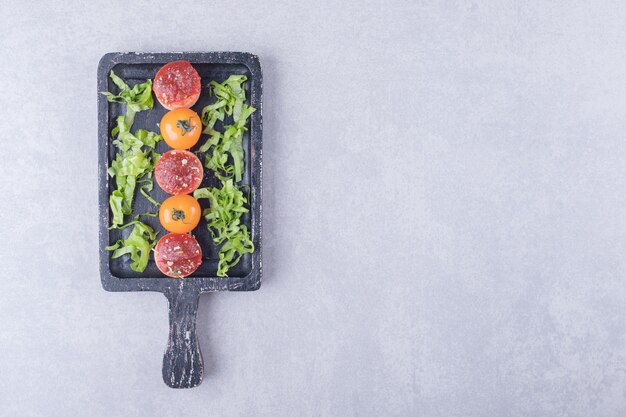 Salsichas saborosas fatiadas com ketchup e tomate no quadro negro.