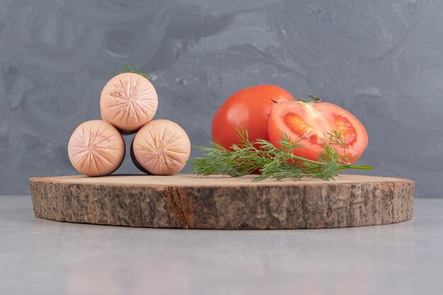 Salsichas saborosas fervidas e tomates na peça de madeira.