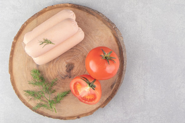 Salsichas saborosas fervidas e tomates na peça de madeira.