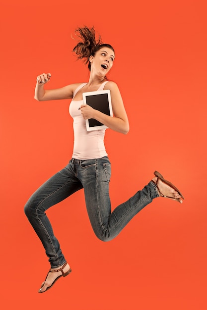 Salto de jovem sobre o estúdio azul usando laptop ou tablet gadget enquanto pula.