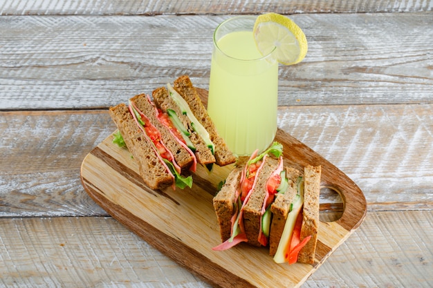 Sanduíche de legumes com queijo, presunto, limonada na tábua de madeira e corte, vista de alto ângulo.