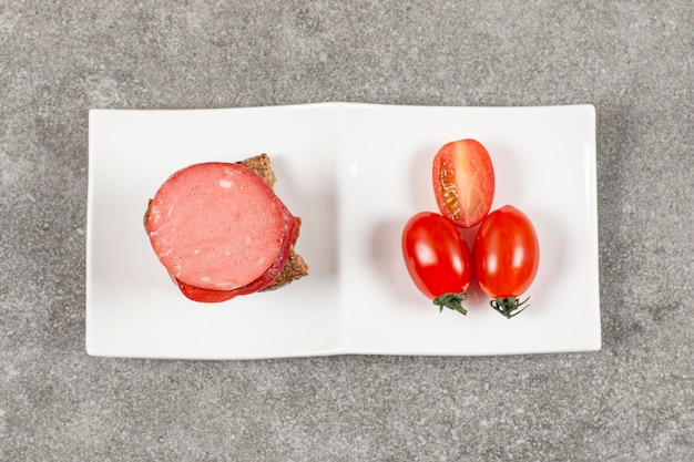 Sanduíche de salame e tomate fresco na chapa branca sobre cinza.