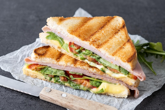 Foto grátis sanduíche panini com presunto, queijo, tomate e rúcula em fundo preto de ardósia