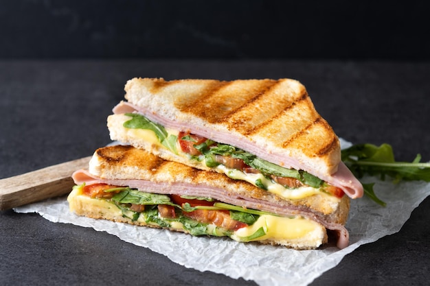 Sanduíche panini com presunto, queijo, tomate e rúcula em fundo preto de ardósia