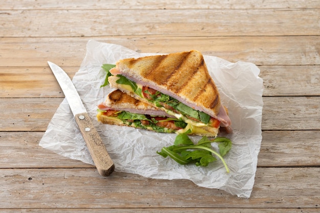 Sanduíche panini com presunto, queijo, tomate e rúcula na mesa de madeira