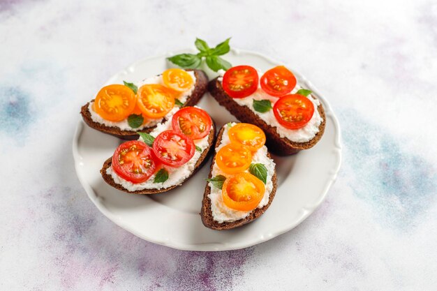 Sanduíches abertos com queijo cottage, tomate cereja e manjericão.