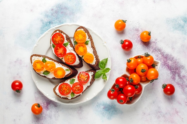 Sanduíches abertos com queijo cottage, tomate cereja e manjericão.