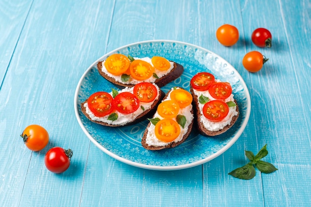 Sanduíches abertos com queijo cottage, tomate cereja e manjericão.