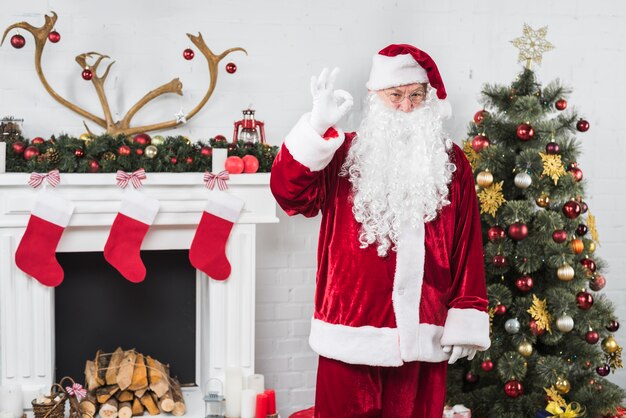 Santa mostrando o gesto bem perto da lareira decorada