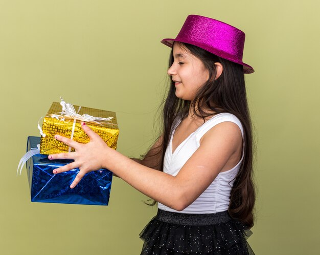 Foto grátis satisfeita jovem caucasiana com chapéu de festa roxo segurando e olhando para caixas de presente isoladas na parede verde oliva com espaço de cópia