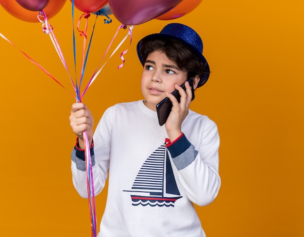 Satisfeito, olhando para o menino com chapéu de festa azul, segurando balões e falando ao telefone