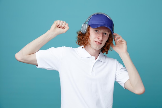 Satisfeito segurando o punho jovem bonitão no boné usando fones de ouvido isolados em fundo azul