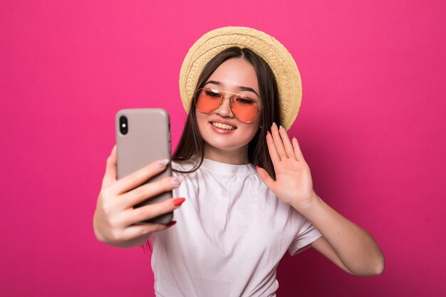 Saudação de mulher asiática no telefone inteligente, na parede rosa