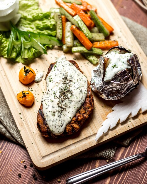 Schnitzel de vista lateral com creme de queijo com batatas assadas em papel alumínio e com legumes em uma placa