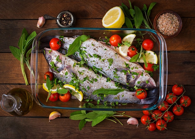 Foto grátis seabass dois cru em uma assadeira com especiarias em uma mesa de madeira velha. vista do topo