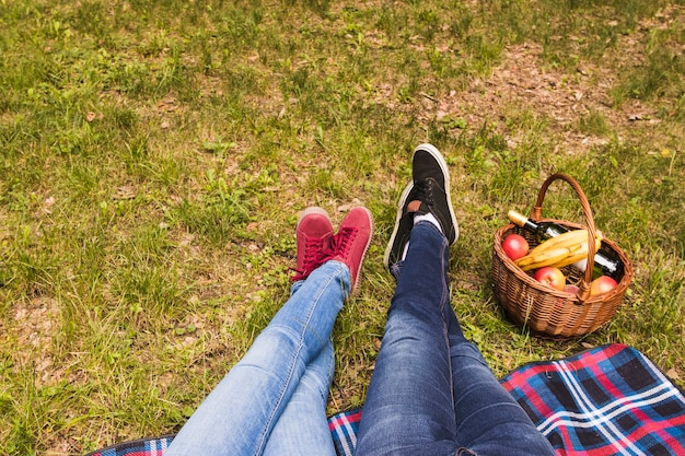 Seção baixa da perna do casal na grama verde com cesta de piquenique