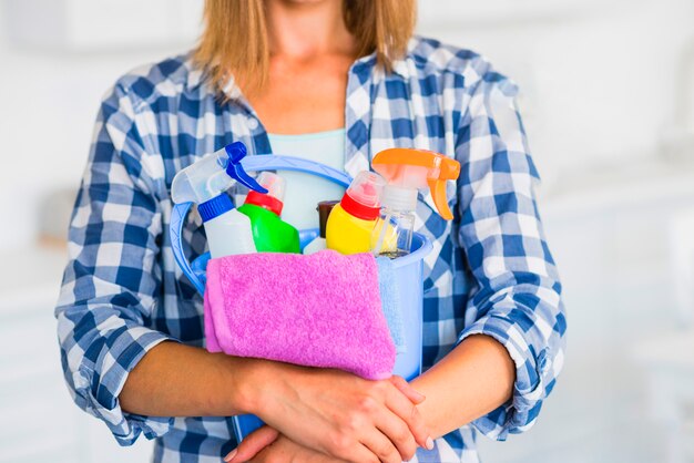 Seção intermediária da mulher segurando equipamentos de limpeza no balde azul