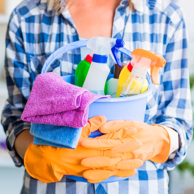 Seção intermediária da mulher segurando equipamentos de limpeza no balde azul