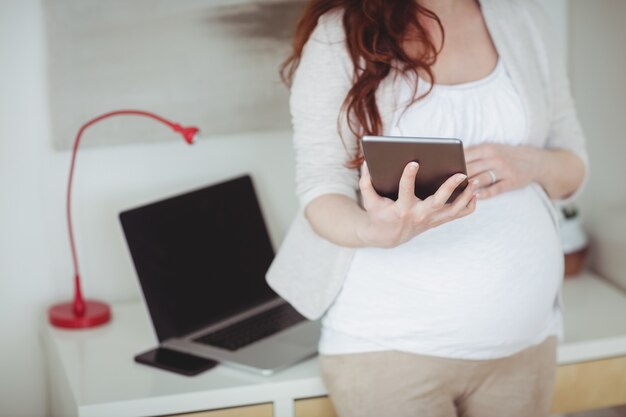 Seção intermediária de mulher grávida usando tablet digital na sala de estudo