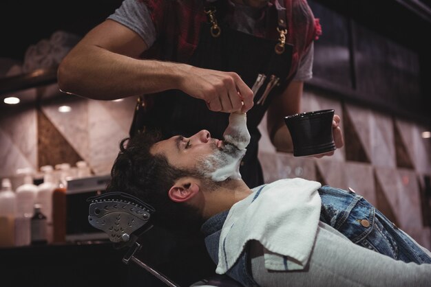 Seção intermediária do barbeiro aplicando creme na barba do cliente