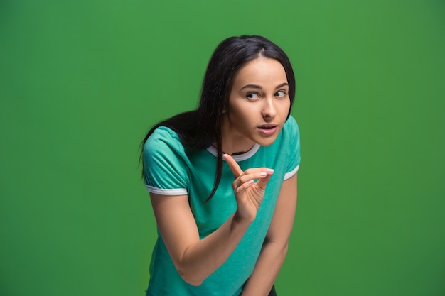 Segredo, conceito de fofoca. Jovem mulher sussurrando um segredo por trás da mão. Mulher de negócios isolada no fundo do estúdio verde na moda. Mulher jovem e emocional. Emoções humanas, conceito de expressão facial.