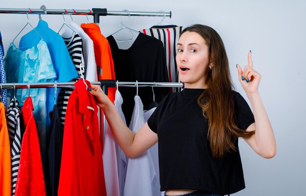 Segurando a blusa menina está apontando para cima com o dedo indicador no fundo da roupa