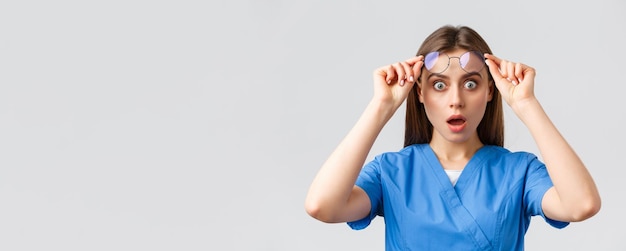Seguro de medicina de trabalhadores de saúde e conceito de pandemia covid19 Surpresa ou chocada enfermeira em avental azul boca aberta e óculos de decolagem atônitos