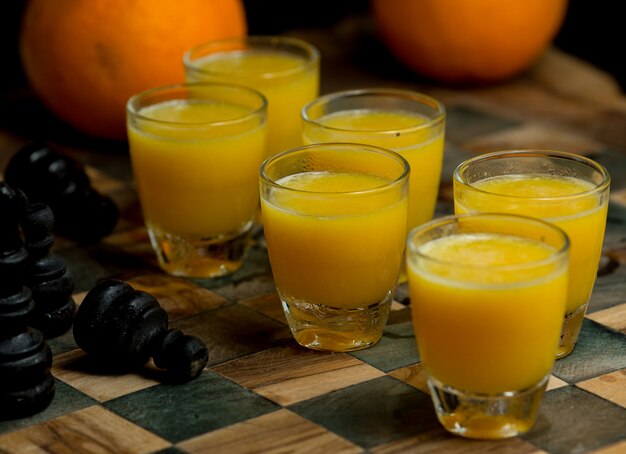 Seis pequenos copos de suco de laranja fresco em uma placa de mate