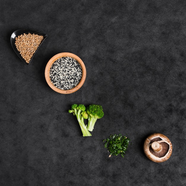 Sementes de coentro; sementes de gergelim; brócolis; cebolinha picada e cogumelo no pano de fundo preto textura