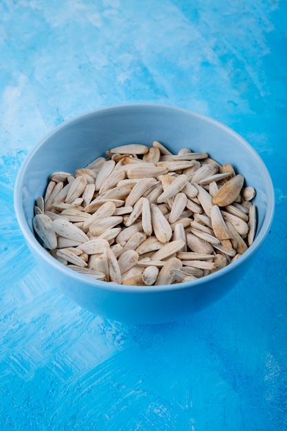 Foto grátis sementes de girassol brancas de vista lateral com sal na tigela sobre fundo azul