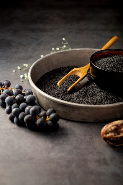 Sementes de papoila em uma placa metálica e uvas em um fundo cinza