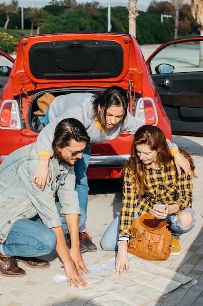 Senhora, abraçando, mulher, com, mochila, e, smartphone, perto, homem, e, olhar, mapa, perto, car