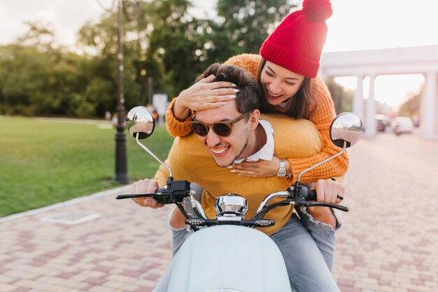 Senhora alegre com manicure da moda brinca com o cabelo do namorado enquanto ele dirige scooter