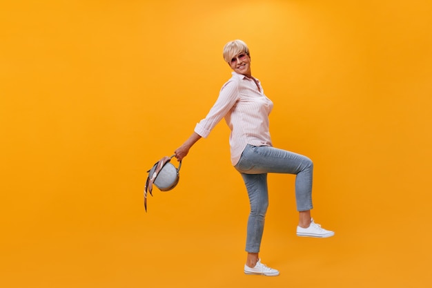 Senhora alegre com roupa de estilo de rua segurando uma bolsa em fundo laranja