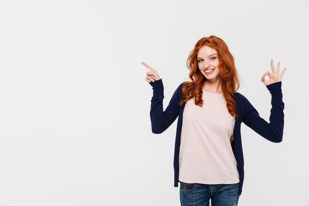 Senhora alegre jovem ruiva mostrando o gesto bem enquanto aponta.