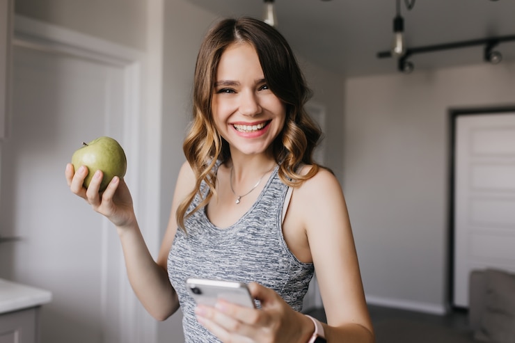 Foto grátis senhora animada com roupas cinza, posando com a apple. mulher loira incrível desfrutando de frutas pela manhã.
