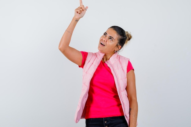 Senhora apontando para cima em camiseta, colete e parecendo confiante