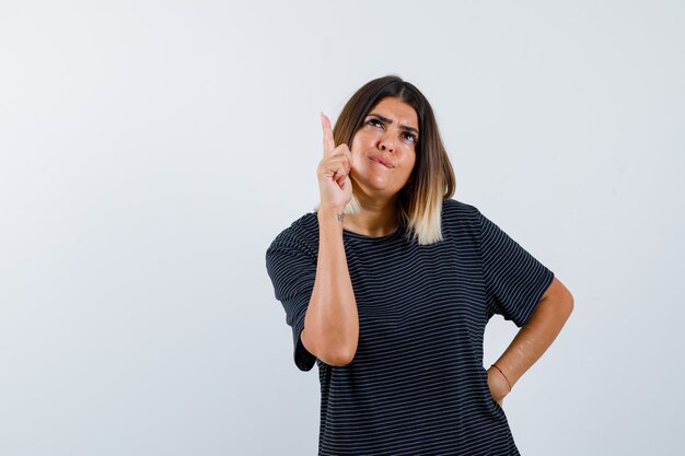 Senhora apontando para cima em uma camiseta preta e parecendo indecisa. vista frontal.