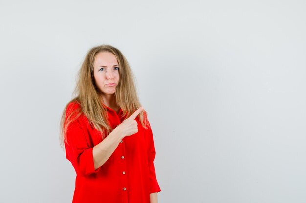 Senhora apontando para o canto superior direito de camisa vermelha e parecendo em dúvida.